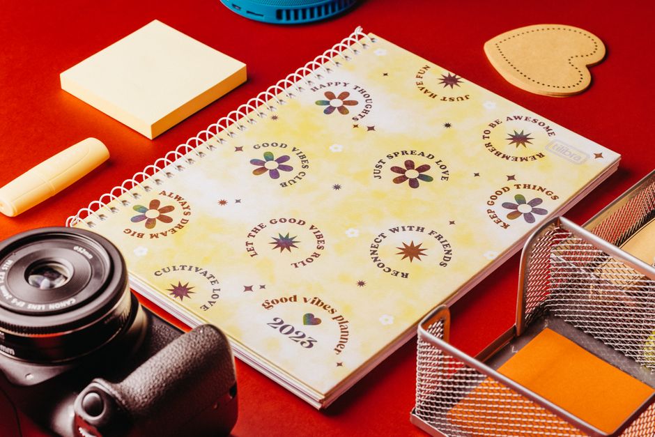 A desk surface features a floral-themed planner for 2023 with motivational phrases such as 'Good Vibes Only', 'Let the Good Vibes Roll', and 'Always Dream Big' in various colors including purple, brow